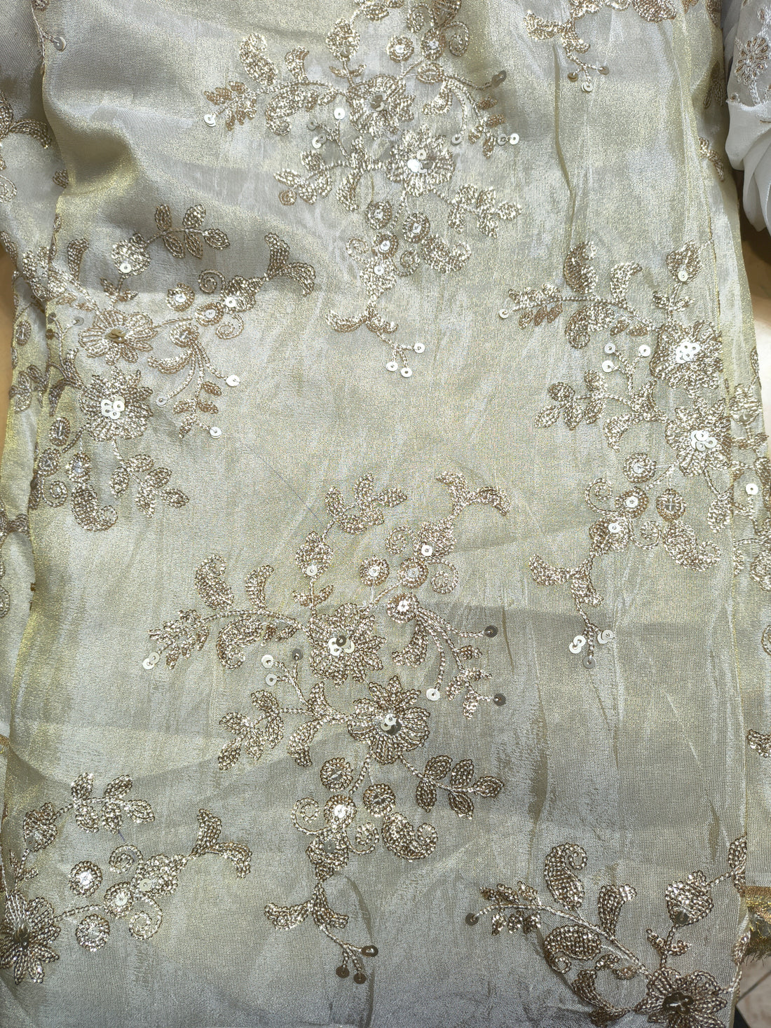 Close-up of silver embroidered fabric with floral patterns on a light background

