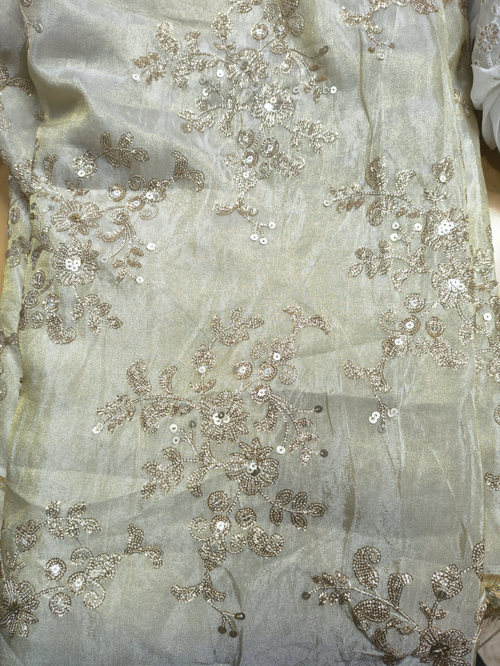 Close-up of silver embroidered fabric with floral patterns on a light background

